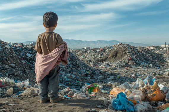 A young boy stands in a garbage dump, looking out at the horizon